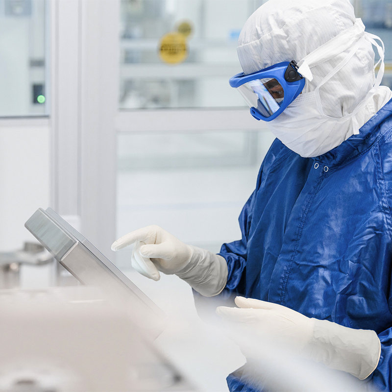American Injectables employee consulting electronic dashboard in full PPE in a clean room. 
